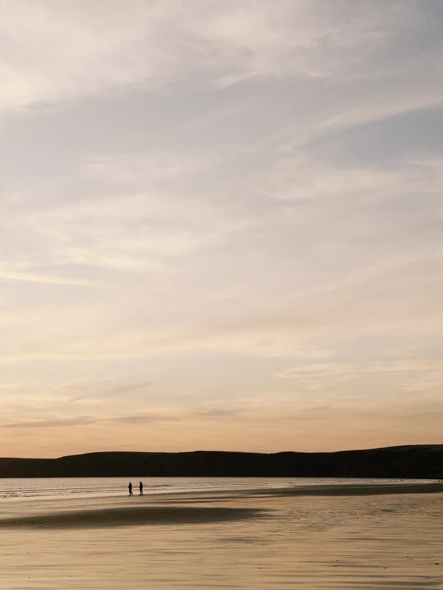 Two people walking across a beach at sunset