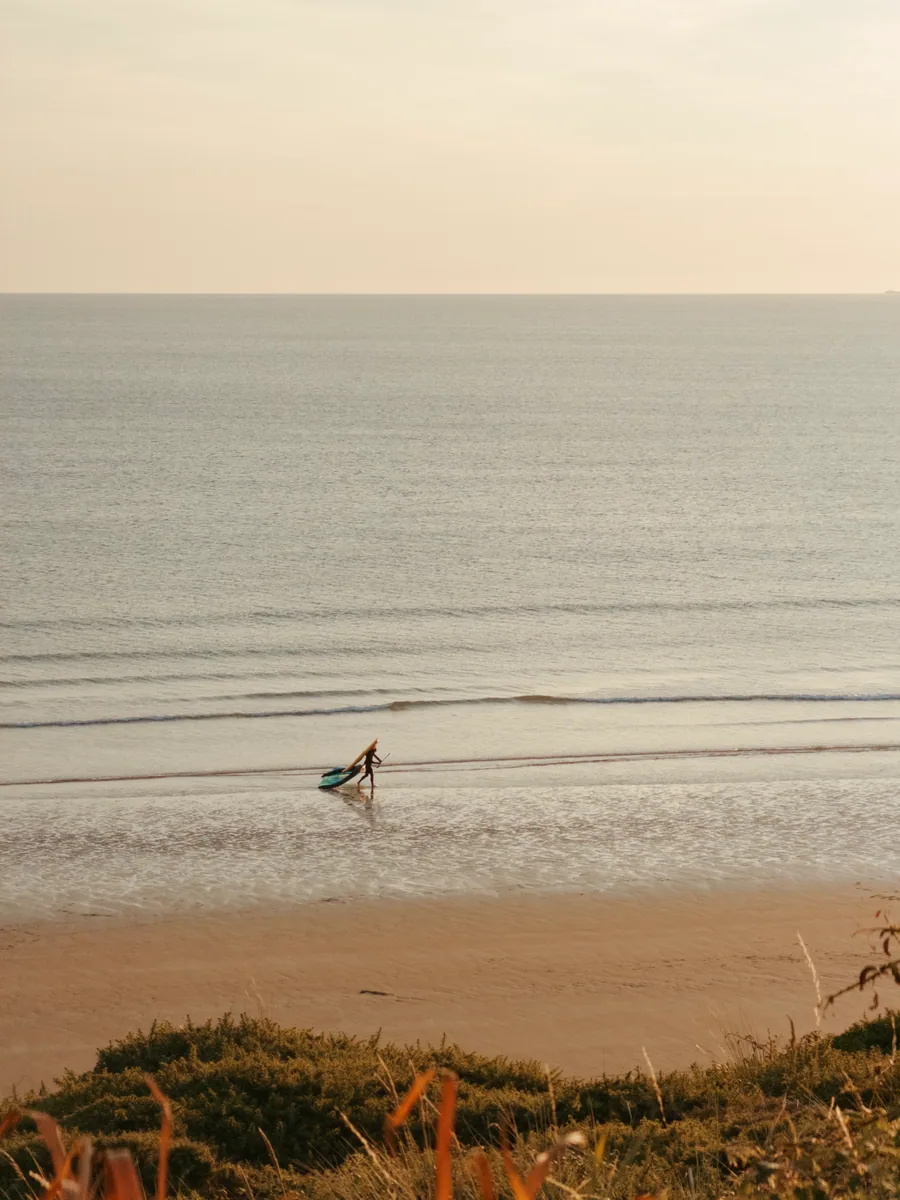 A surfer walking along the shoreline