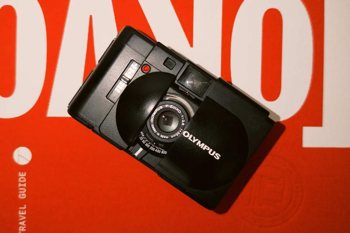 An Olympus compact film camera resting on a red and white book.