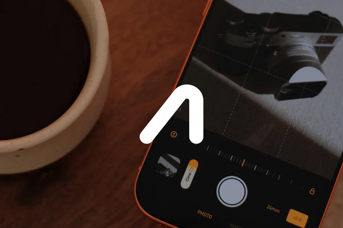 An iPhone running the Analogue camera app on a wooden table, aimed at a Fujifilm camera beside a cup of coffee
